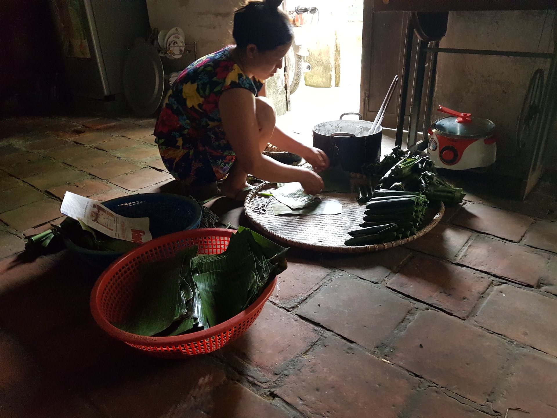 Mẹ ngồi gói bánh lá răng bừa bên mẹt tre, cạnh nồi bột và rổ lá chuối